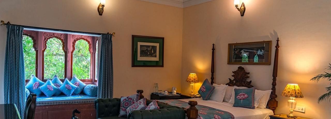 Deluxe Room Featuring a four-poster bed, a window seating area with decorative cushions, and elegant decor - Khas Bagh, Jaipur