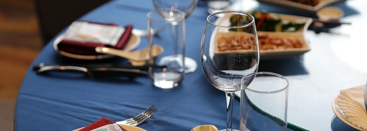 A close up shot of a round dining table with sparkly glassware and cutlery arranged on it.