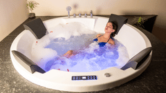 A woman with her eyes closed relaxing in a large, round bathtub with water and rose petals.