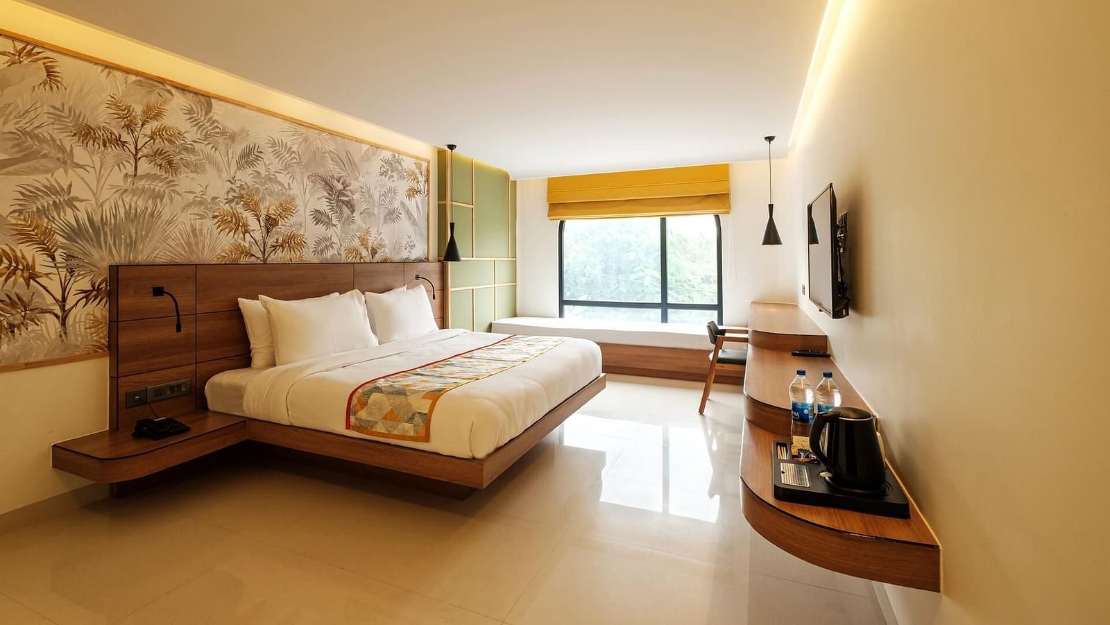 A spacious room at Indie Stays, Jaipur, with a large bed featuring a wooden headboard, a wall-mounted TV with a wooden shelf below, and a large window with an alcove.