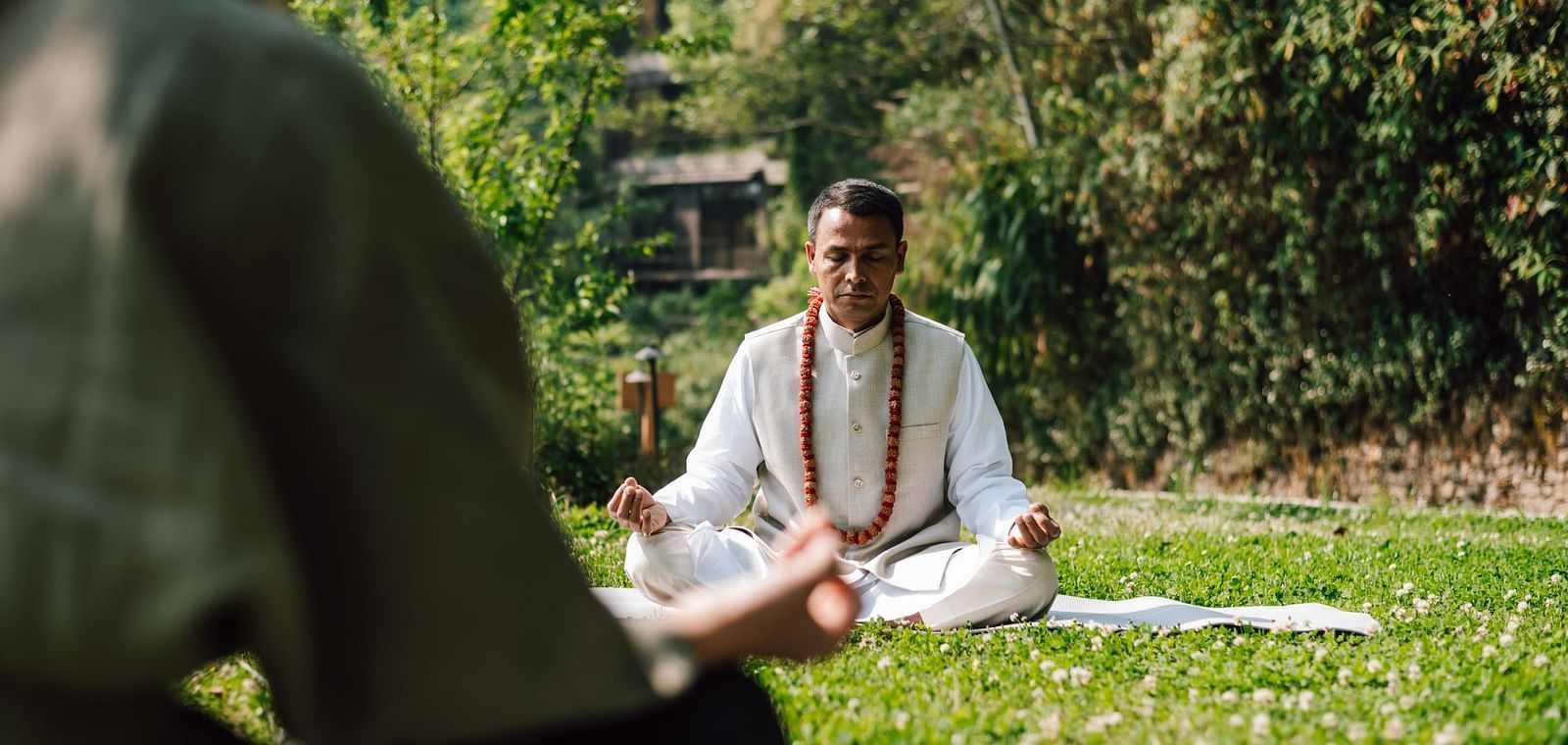 Person meditating outdoors in a peaceful garden setting, surrounded by greenery.
