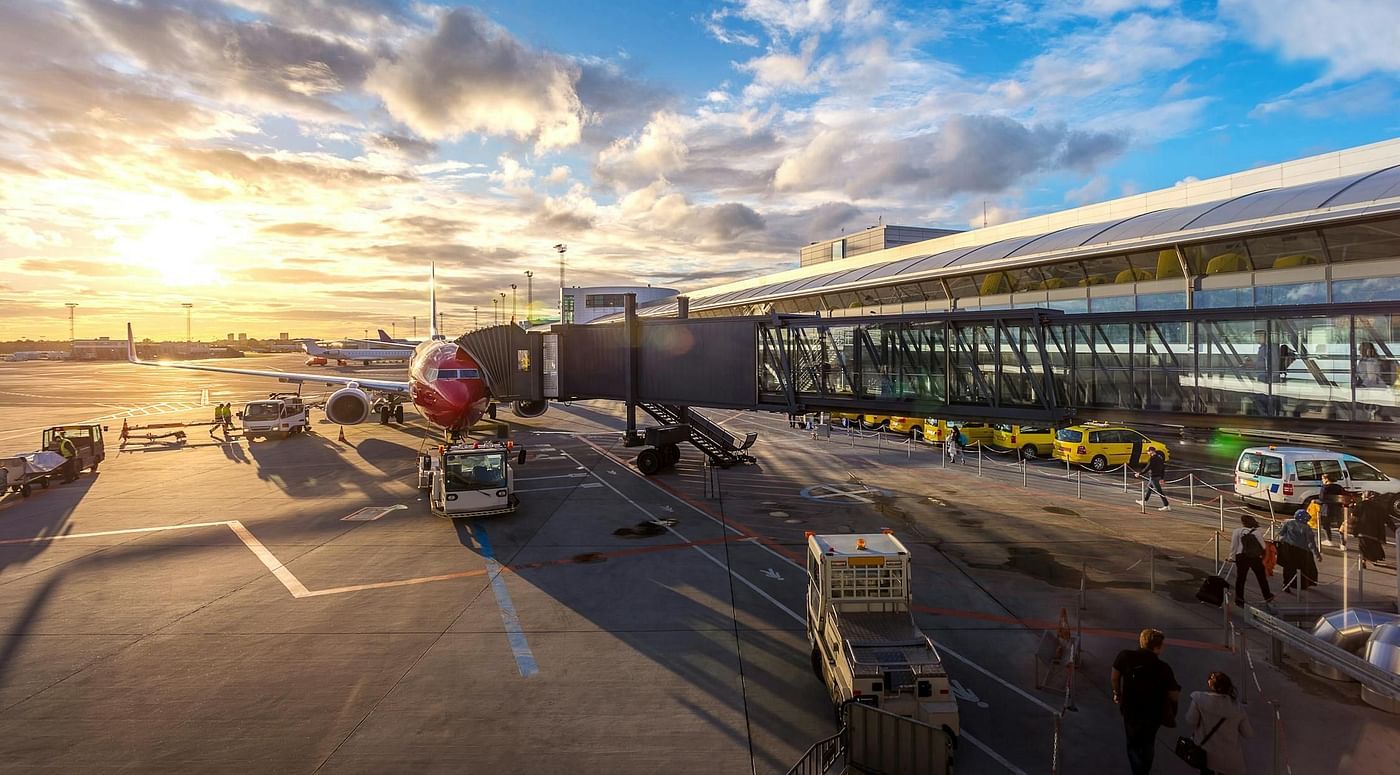 An airport terminal with airplanes visible through large windows and a bright, sunny sky outside.