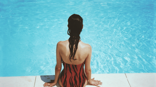 A girl sitting by the edge of a swimming pool, dipping her feet in the water.