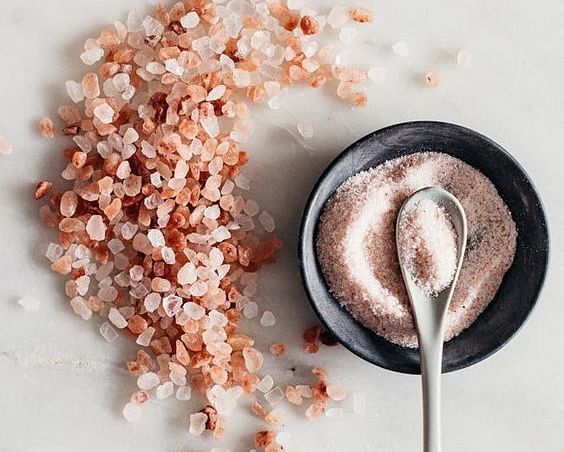 Pink face cream in a black bowl with a spoon, surrounded by pink Himalayan salt crystals.