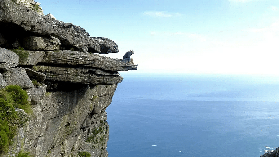 A person sitting on the edge of a cliff overlooking a coastal city and the ocean.