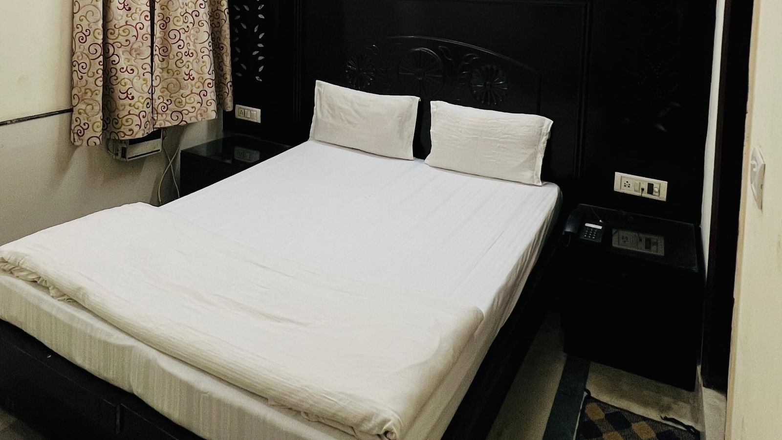 A simple and clean standard room with a comfortable bed, a ceiling fan, and dark wood furniture, offering basic amenities for a restful stay at Hotel City Palace DX.