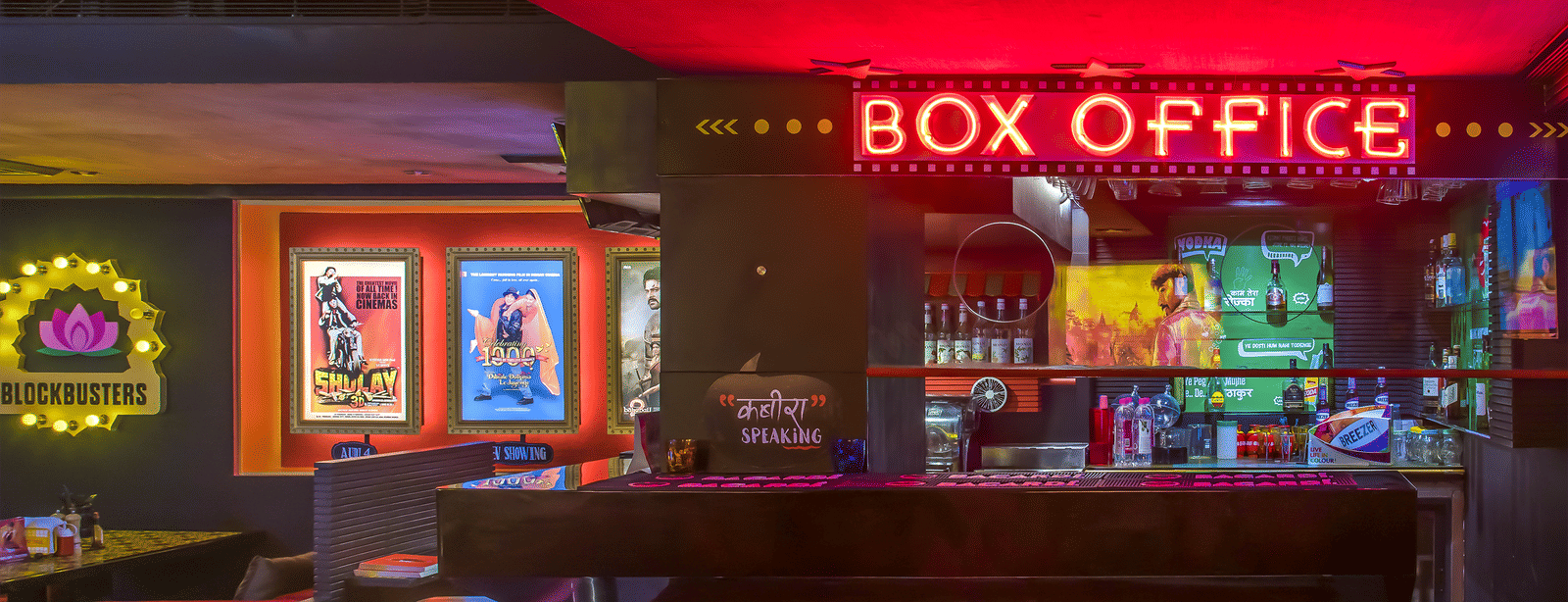 A bar counter with a glowing 'BOX OFFICE' sign, red lights and wall posters at Infiniti Hotel, Indore.