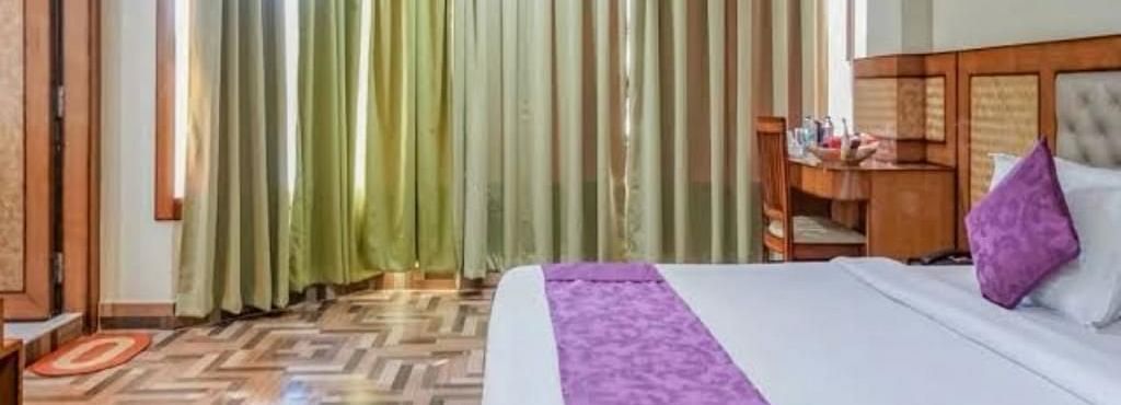 A spacious bedroom with rich wooden flooring, green drapes, and a purple-accented bed for a cosy stay - Pemaling Lords Eco Inn Guwahati