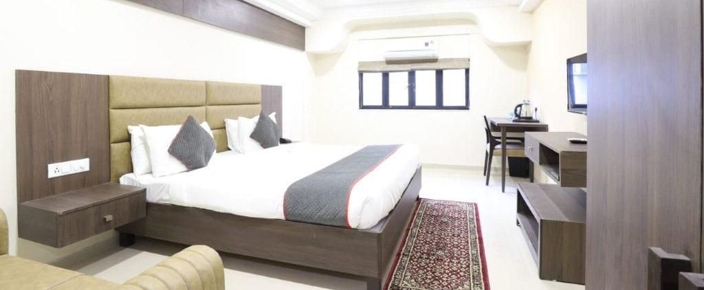 Side view of the Premium Room with bright lighting at Pravasa Stay, Ahmedabad (Alba Premier) featuring a 4-panelled window at the far end of the room. 