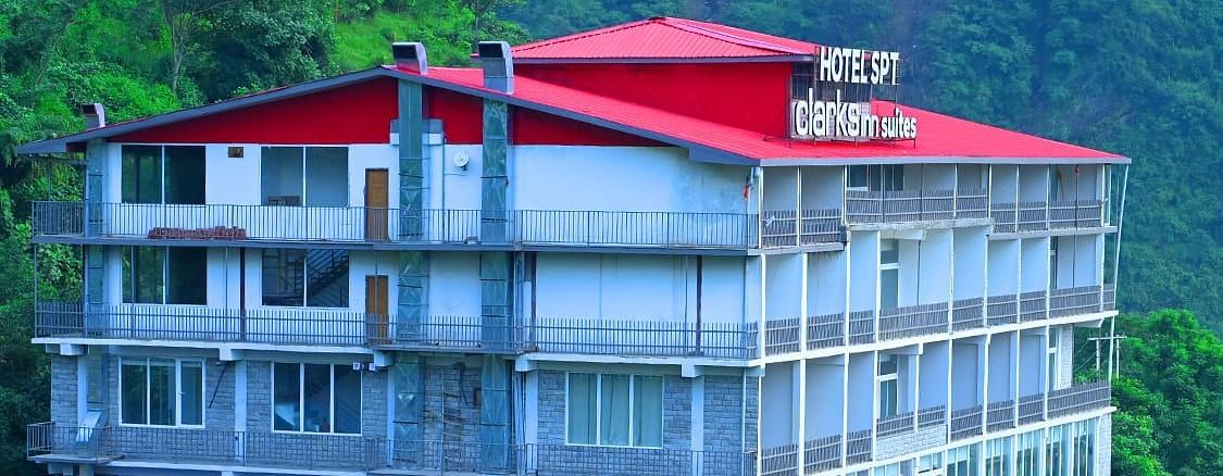 Facade of SPT Clarks Inn Suites, Mandi amidst lush greenery with a glimpse of a mountain in the bakcground