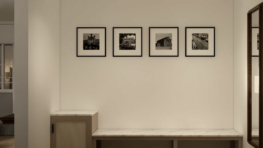 A minimalist hallway featuring a long wooden bench under 4 square framed pictures on a white wall at Shilton Suites, Bengaluru.