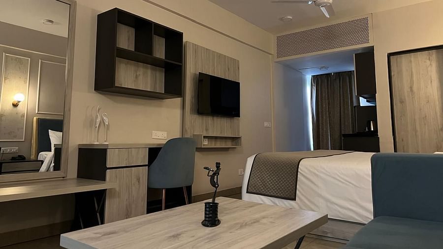 A spacious room featuring a large bed, a wooden table, and a study table with a chair in front of the wall, along with a wall-mounted TV at Urban Suites by BluSalzz, Jaipur.