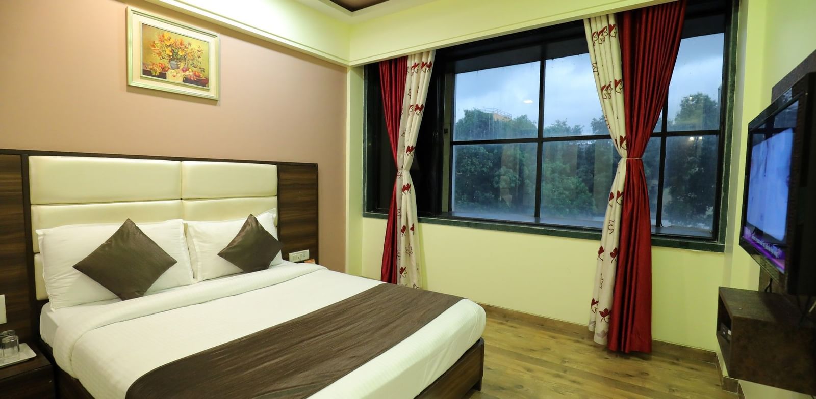 An Executive Room at Krushnai Resort with a white bed, brown accents, and a window with red curtains.