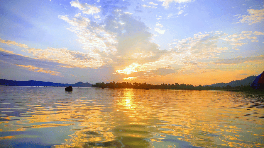 Sunset over lake with calm waters reflecting the sky and distant trees.