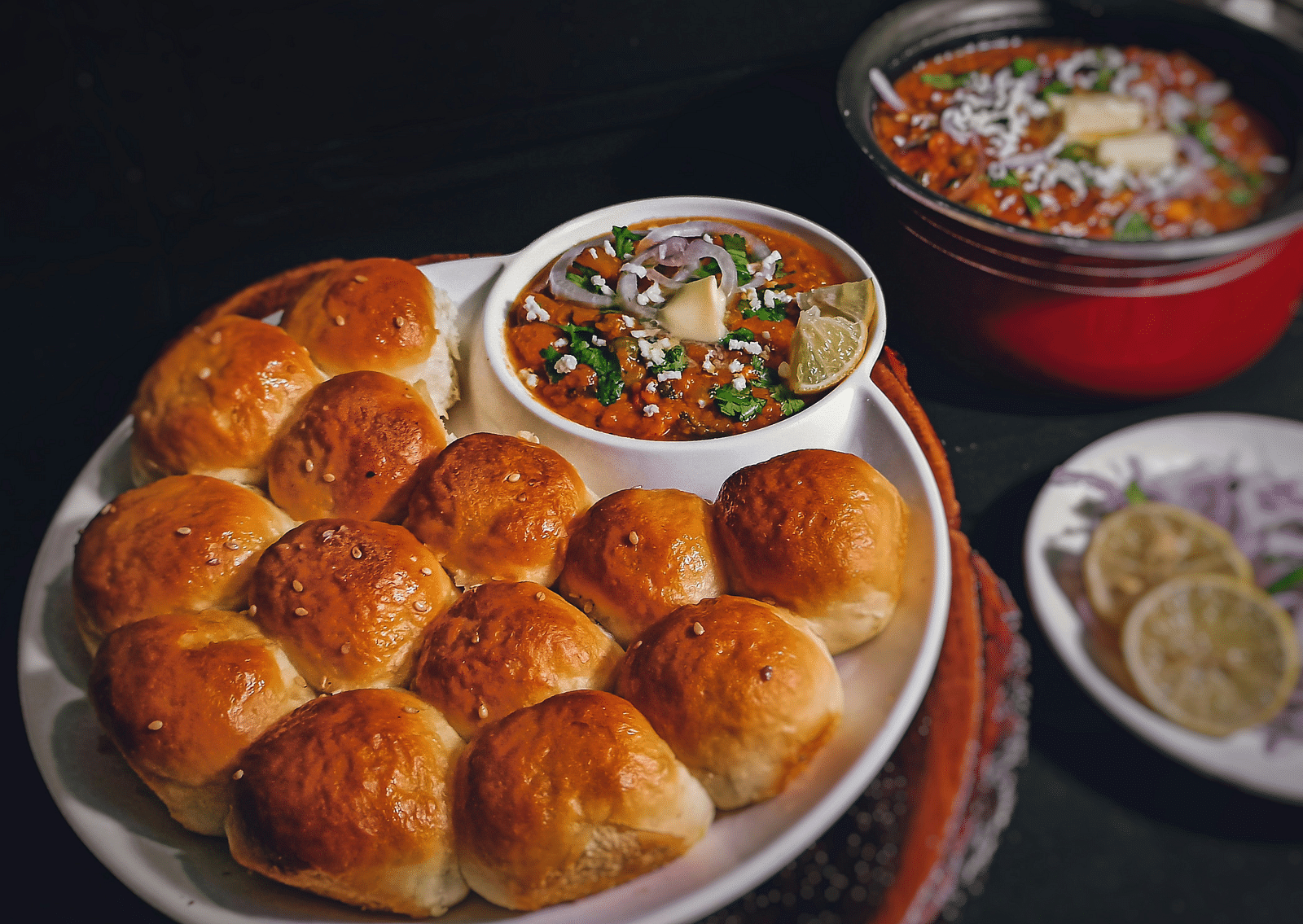 An overview of a plate with many pav and a cup holding bhaji and lime slices next to it.