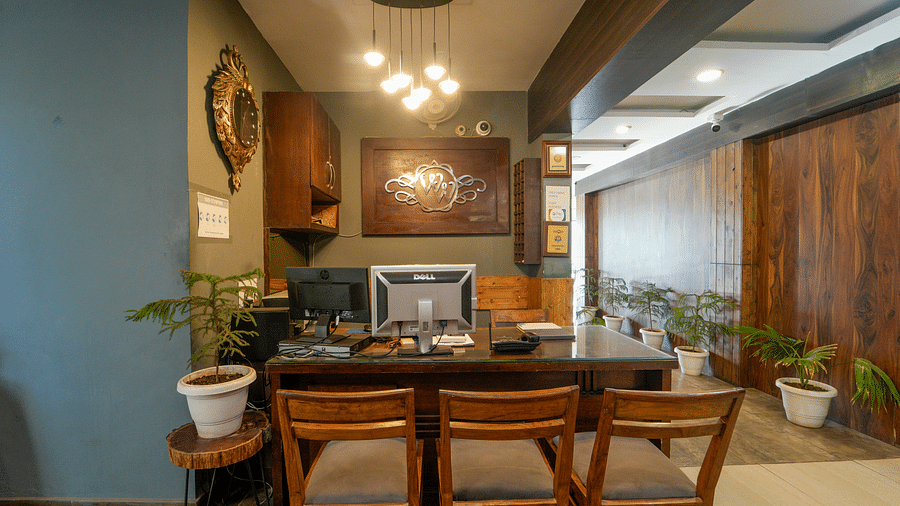 A close up shot of the reception desk, a desktop, three chairs, and plants planted in pots kept for decoration - DLS Whispering Winds