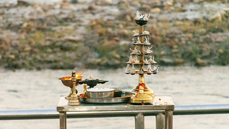 Traditional Indian puja setup on a riverside platform, featuring brass lamps, a kalash, and ritual items.
