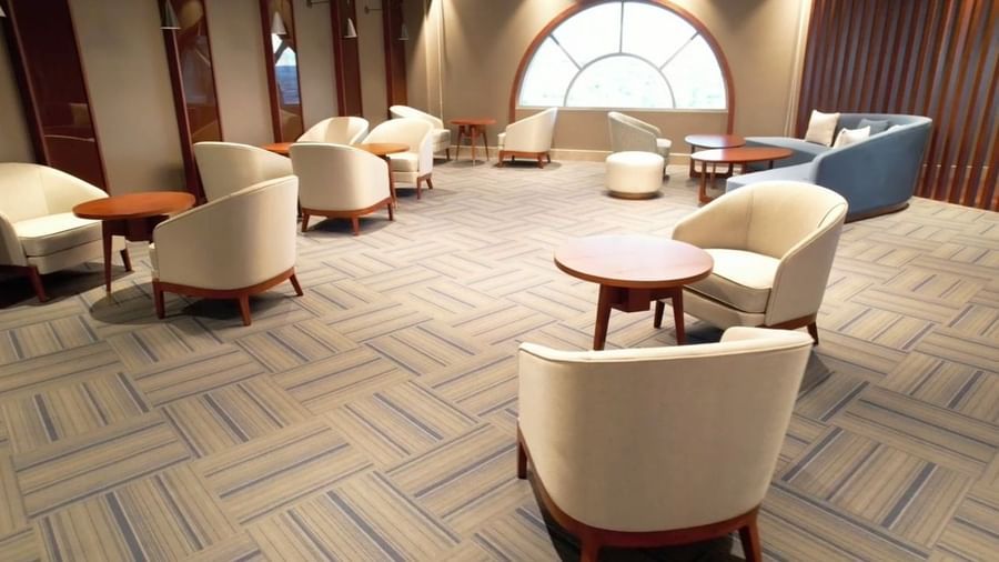 The seating area in VIP Lounge featuring soft beige chairs, wooden tables, and arched window backdrop - Serene Sarovar Premiere Hargeisa