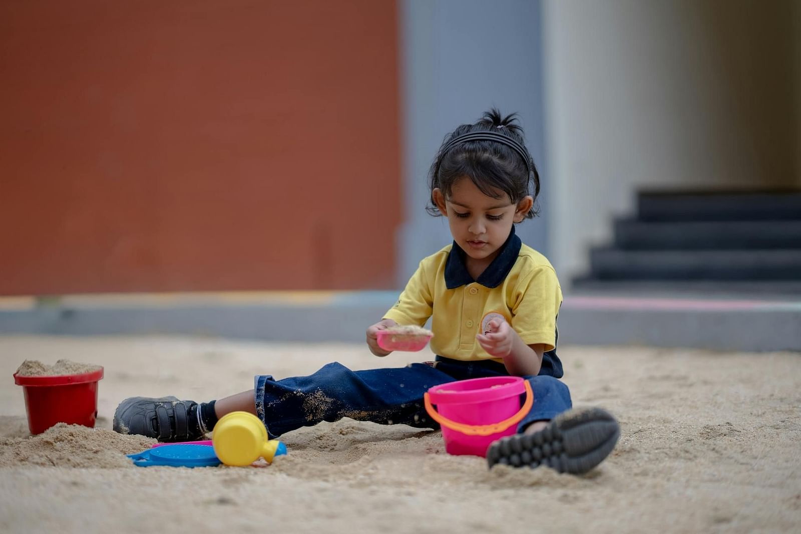 A young girl playing with sand toys in an outdoor play area, sitting barefoot with colourful buckets and spades around her—capturing the joyful atmosphere of our child-friendly hotel in Kodaikanal.