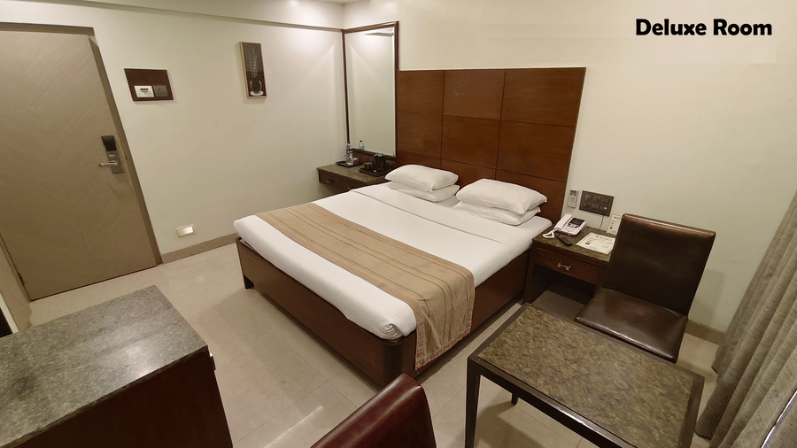A bedroom with a bed in the centre, 2 matching nightstands, a big wall mirror and  a tiled floor | Kings International Juhu