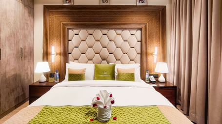 Junior Suite bedroom at The Meriton, New Delhi featuring plush bedding and warm lighting