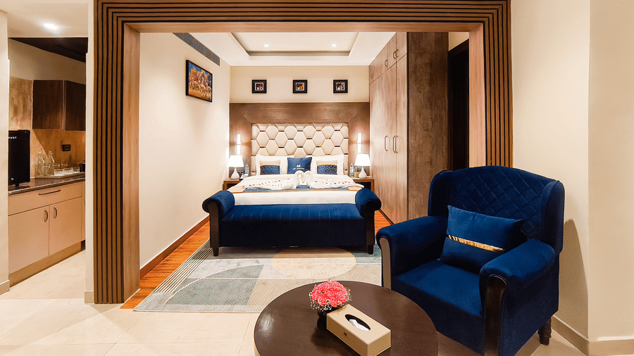 A spacious Standard Room at The Meriton featuring a cosy seating area, plush armchairs, modern interiors, and a comfortable bed for a relaxing stay.