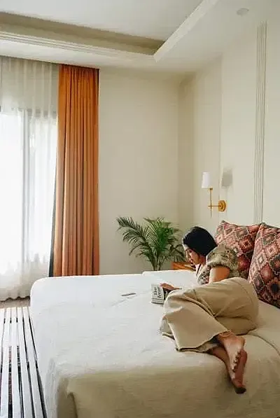 A guest sitting on a bed in a room at Karma Chalets with long curtains and indoor plants.