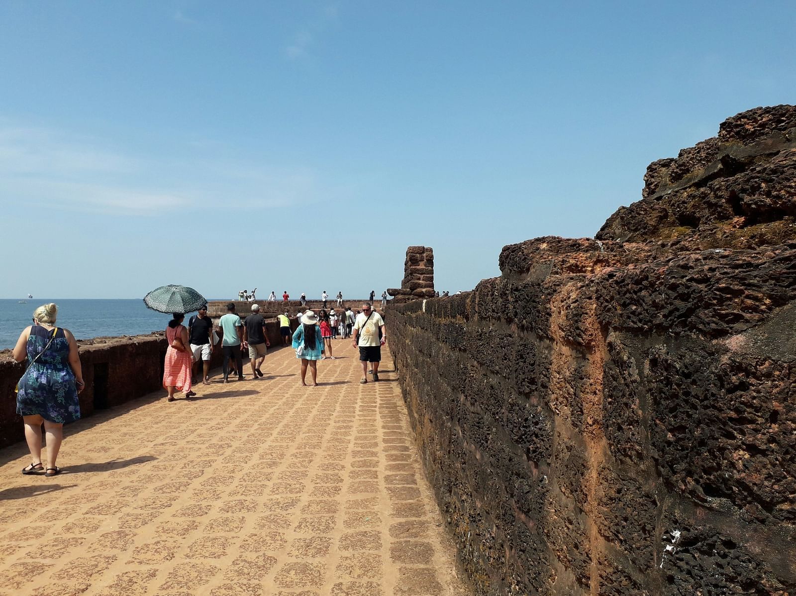 People walking on a pathway next to Fort Aguada with blue sky in the background