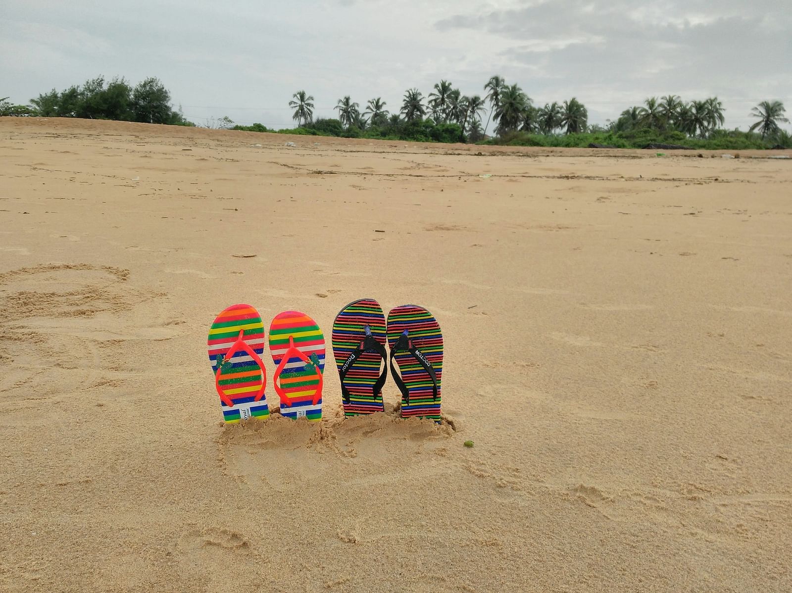two sets of slippers buried halfway in Candolim Beach with trees in the background