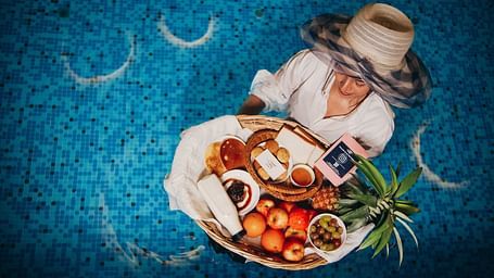 An overhead of a woman enjoying a dish with meat and vegetables in a swimming pool | Mansha Hotels