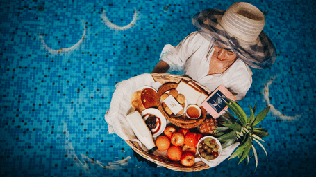 An overhead of a woman enjoying a dish with meat and vegetables in a swimming pool | Mansha Hotels
