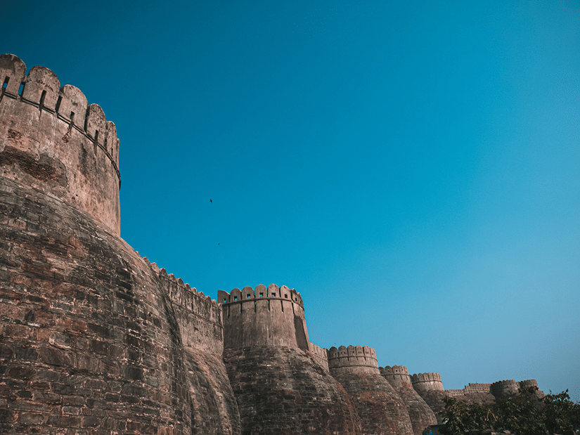 Kumbhalgarh Fort's towering stone ramparts rising against a clear blue sky, showcasing its imposing historic architecture
