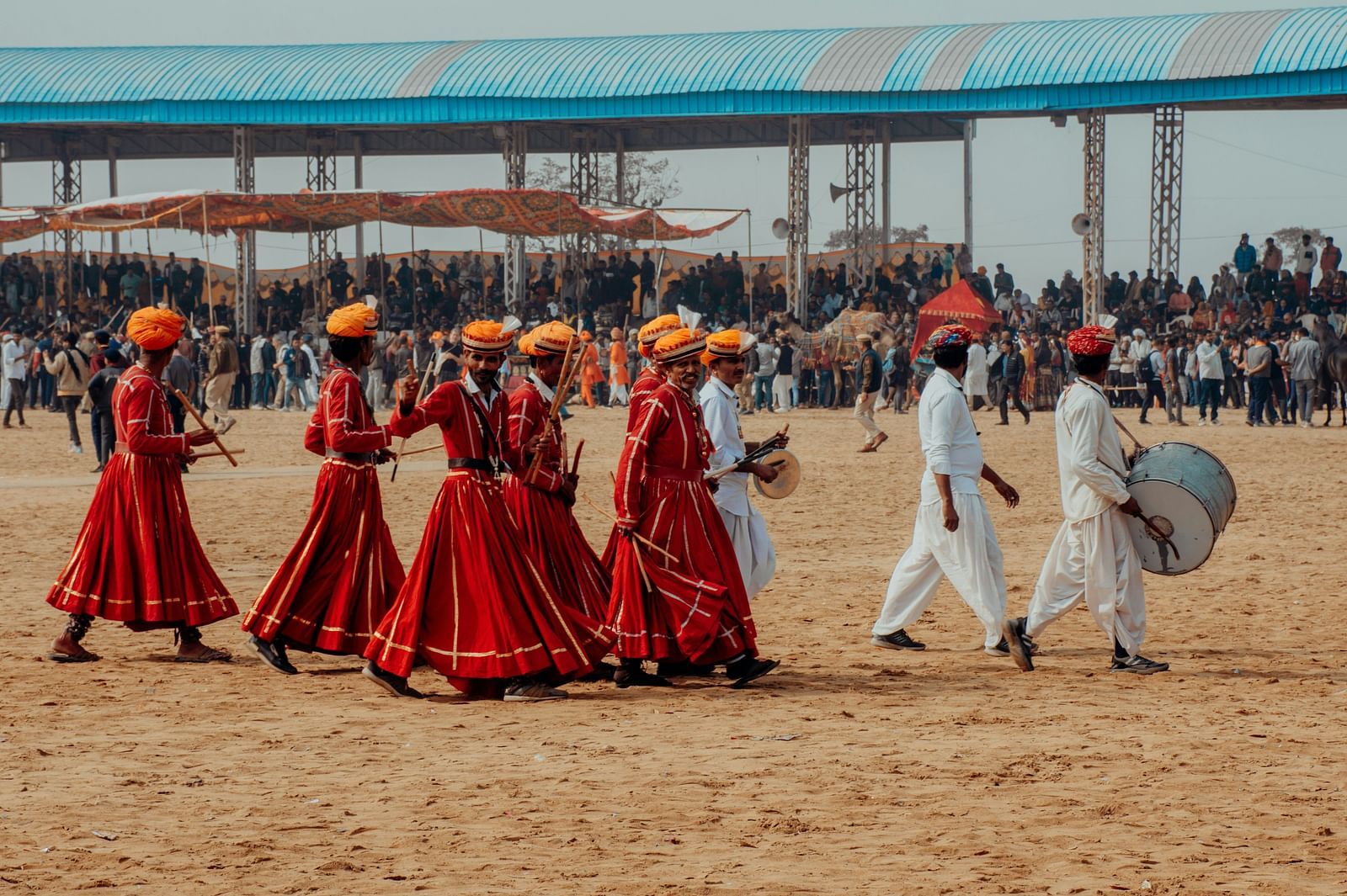 Group of people in traditional clothing walking across a sandy field.