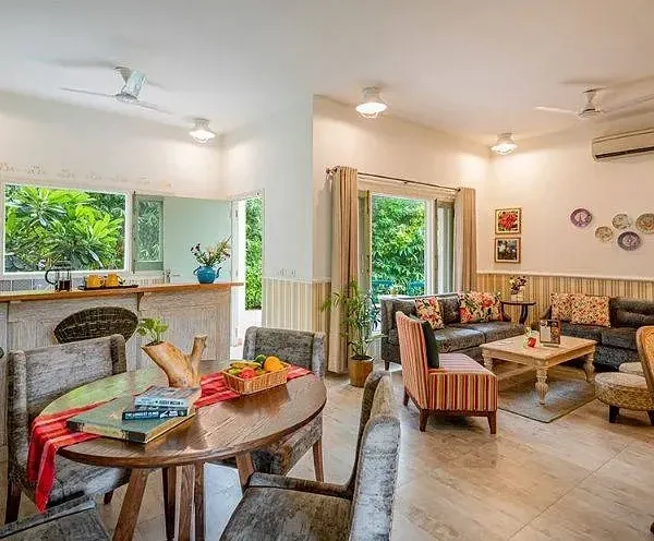 Cosy dining area with rustic wooden furniture, colourful cushions, and windows opening to a green view at Karma Chalets.