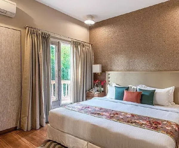 Elegant bedroom with a large bed, neutral-toned walls, full-length curtains, and a window overlooking greenery at Karma Chalets.