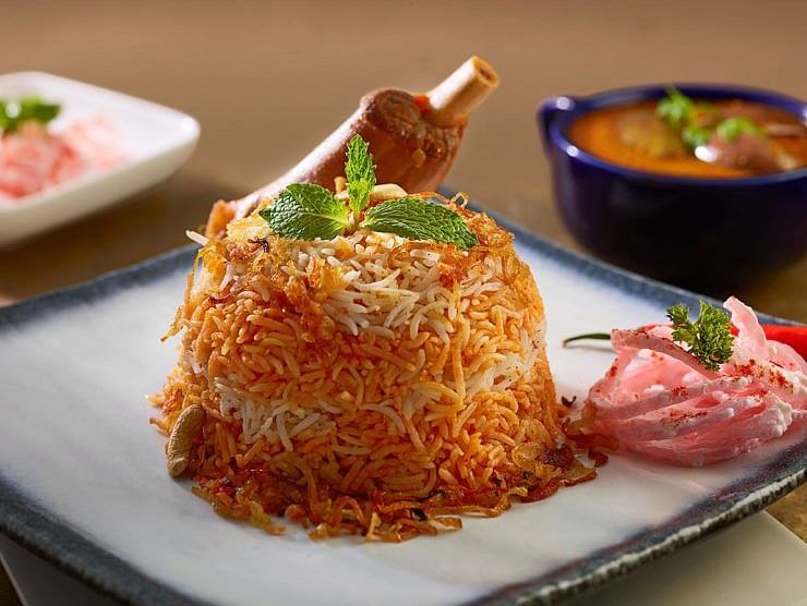 Plate of biryani served with raita and a side of curry in bowls.