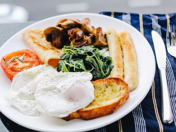 Plate of English breakfast with poached eggs, toast, spinach, mushrooms, and tomatoes.