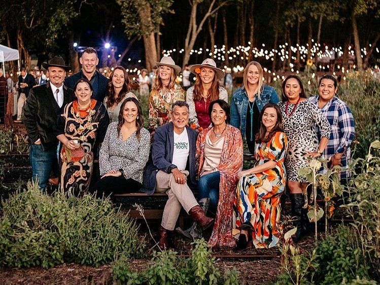 A group of people, including friends and family, posing together outdoors in a garden, smiling for the camera.