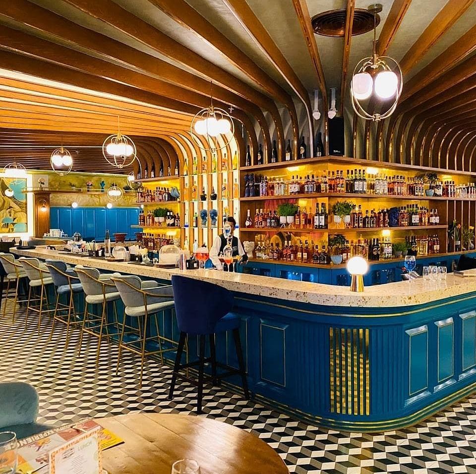 An image of a bar featuring a counter table, chairs, and a shelf where liquor items are placed - Themis Barbecue House, Panipat