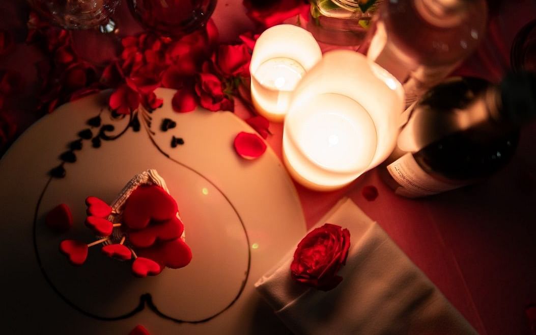 A romantic dining arrangement with a candle and a bottle of wine placed on a table with a dark pink table cloth