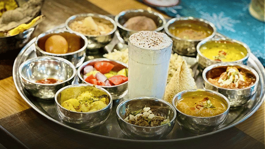 A close-up shot of an elaborate thali showcasing a well-plated Rajasthani thali with a glass of buttermilk in the centre - Amantra Comfort Hotel
