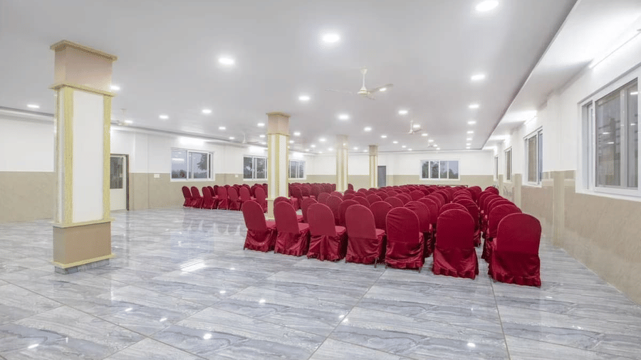 Back view of a spacious banquet hall at Siri Ambari Resorts and Spa, featuring red-covered chairs and bright lighting.