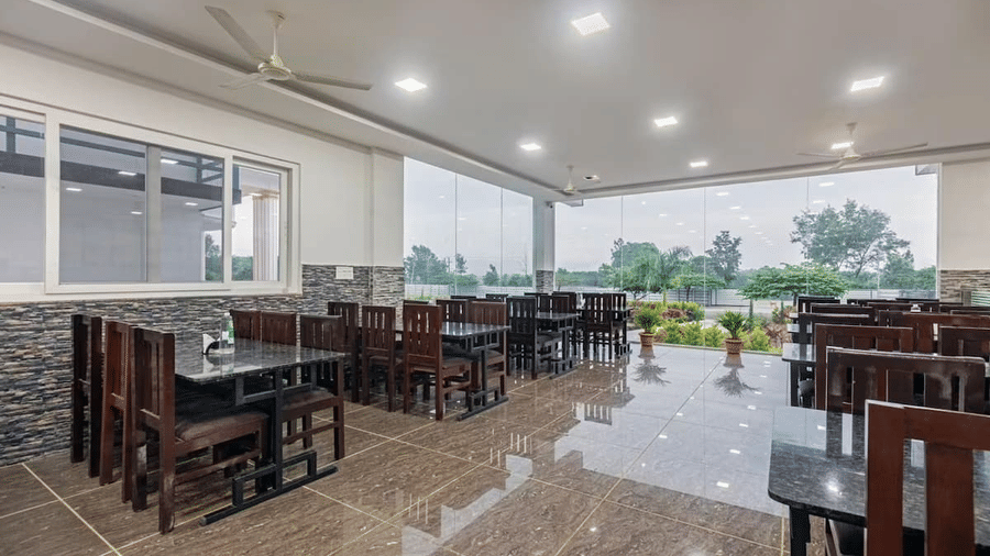 Well-lit restaurant with large windows offering scenic views and comfortable wooden seating at Siri Ambari Resorts and Spa.