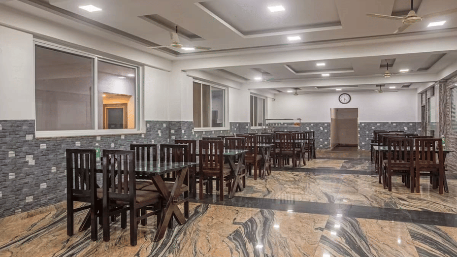 Indoor dining area with polished flooring and neatly arranged wooden tables and chairs at Siri Ambari Resorts and Spa.