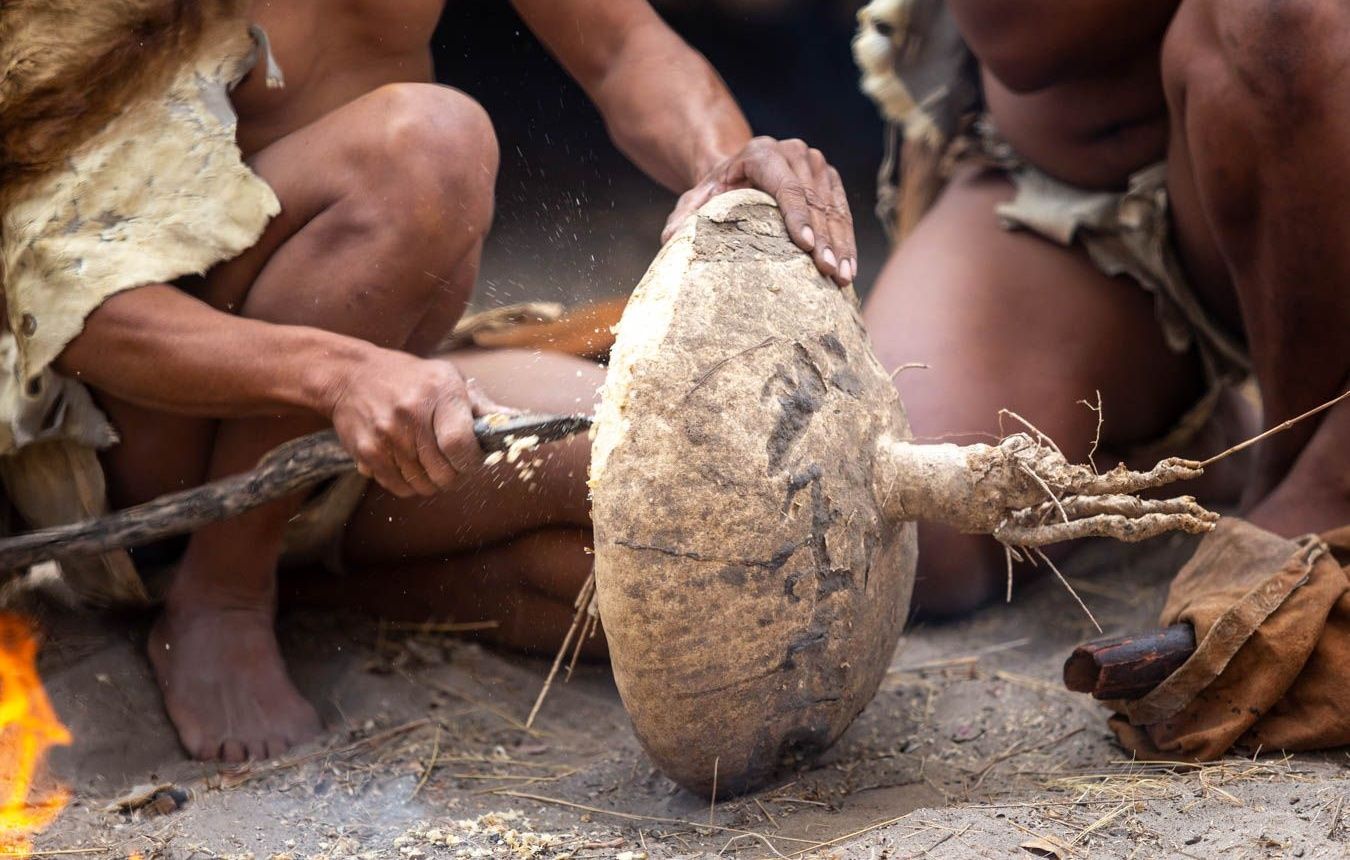 Individuals using a large mortar and pestle by a fire.