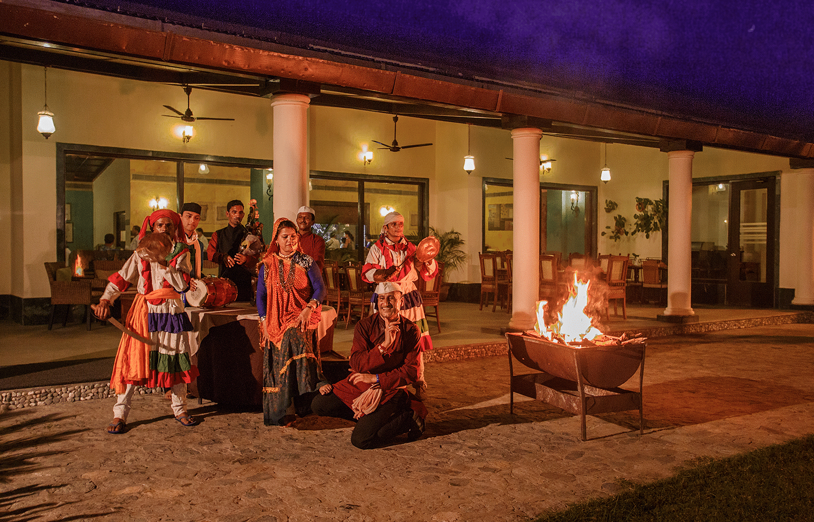 An image of a group of people in traditional clothes dancing and playing musical instruments near a bonfire 