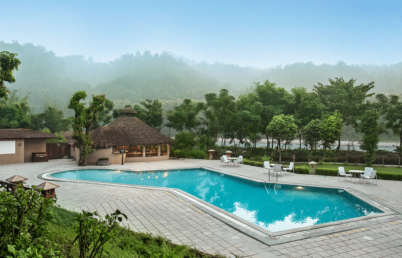 An image of a swimming pool surrounded by trees and huts