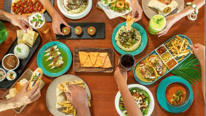 Many hands reaching for various colourful dishes and drinks on a large wooden table at Lamari Siargao.