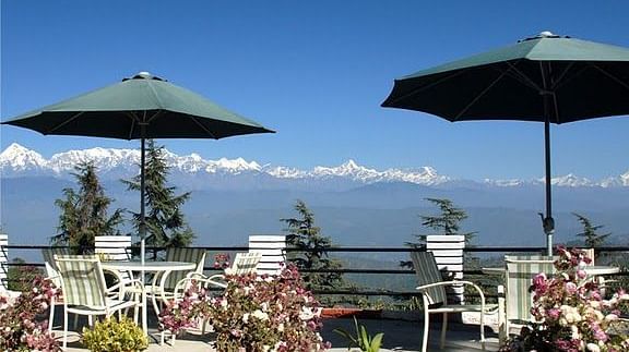 two tables set outside with umbrellas perched on them for providing shade and views of the beautiful hills in the distance - Sun N Snow Inn, Kausani