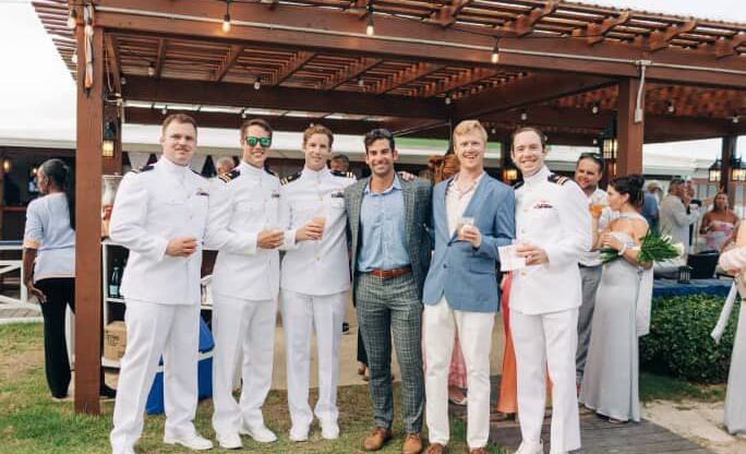 Group of men and women, some in suits and some in white shirts, pose for a photo under a wood pavilion at Abaco Inn.